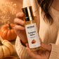 Person holding a bottle of Soft Petalz Pumpkin Spice Body Oil with pumpkins and cinnamon sticks in the background.